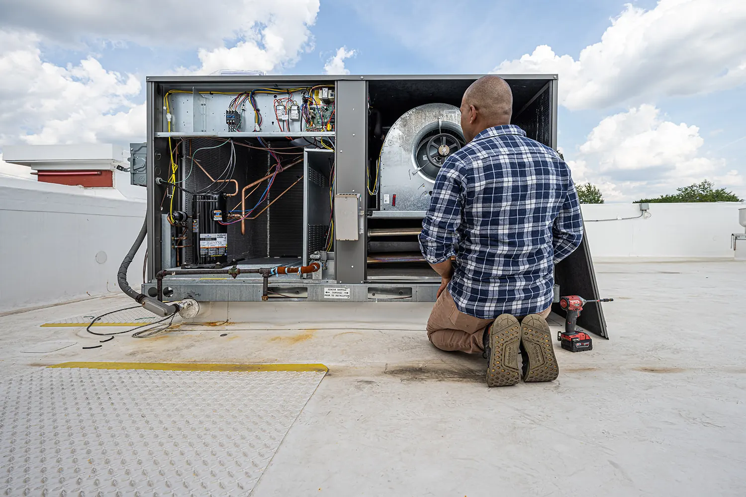 A technician kneeling at an open rooftop unit, working inside it