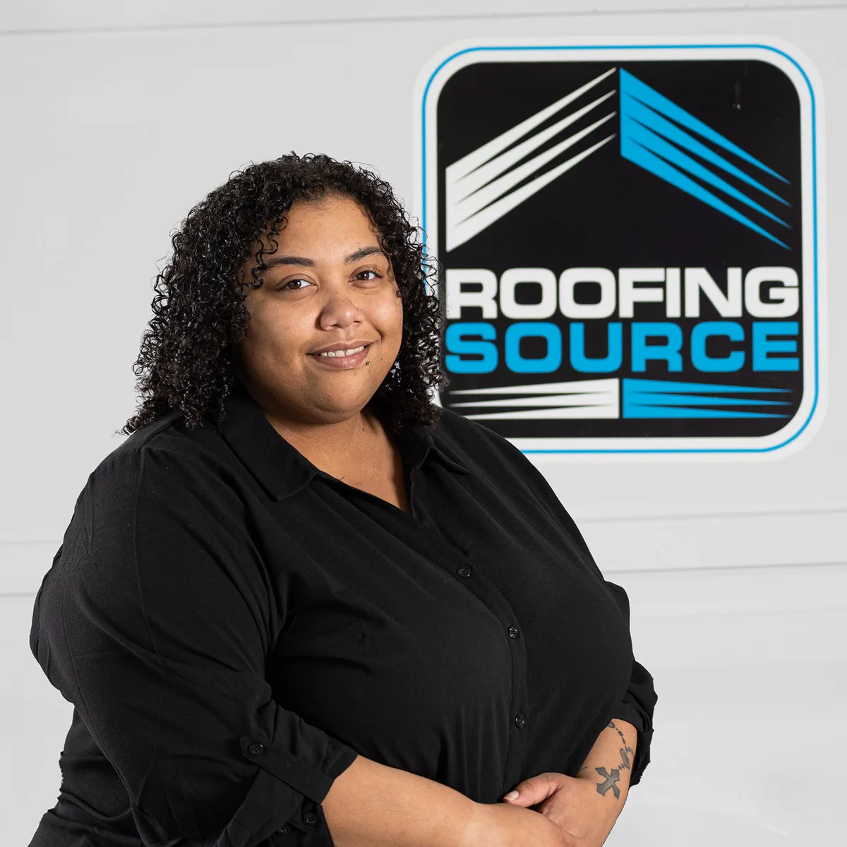A RoofingSource teammate in a black shirt smiling in front of the company logo
