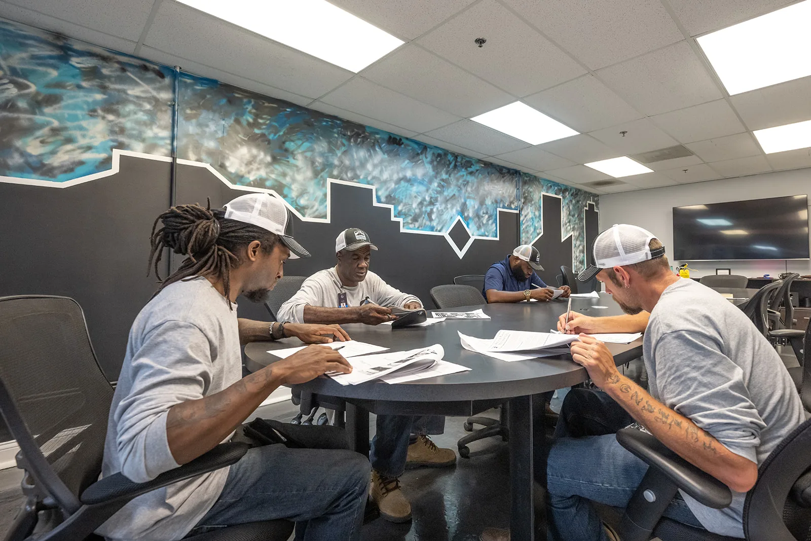 Four RoofingSource teammates working through plans at a table in the training room