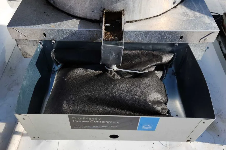 A grease containment box fitted beneath a rooftop exhaust fan, its absorbent pads in place