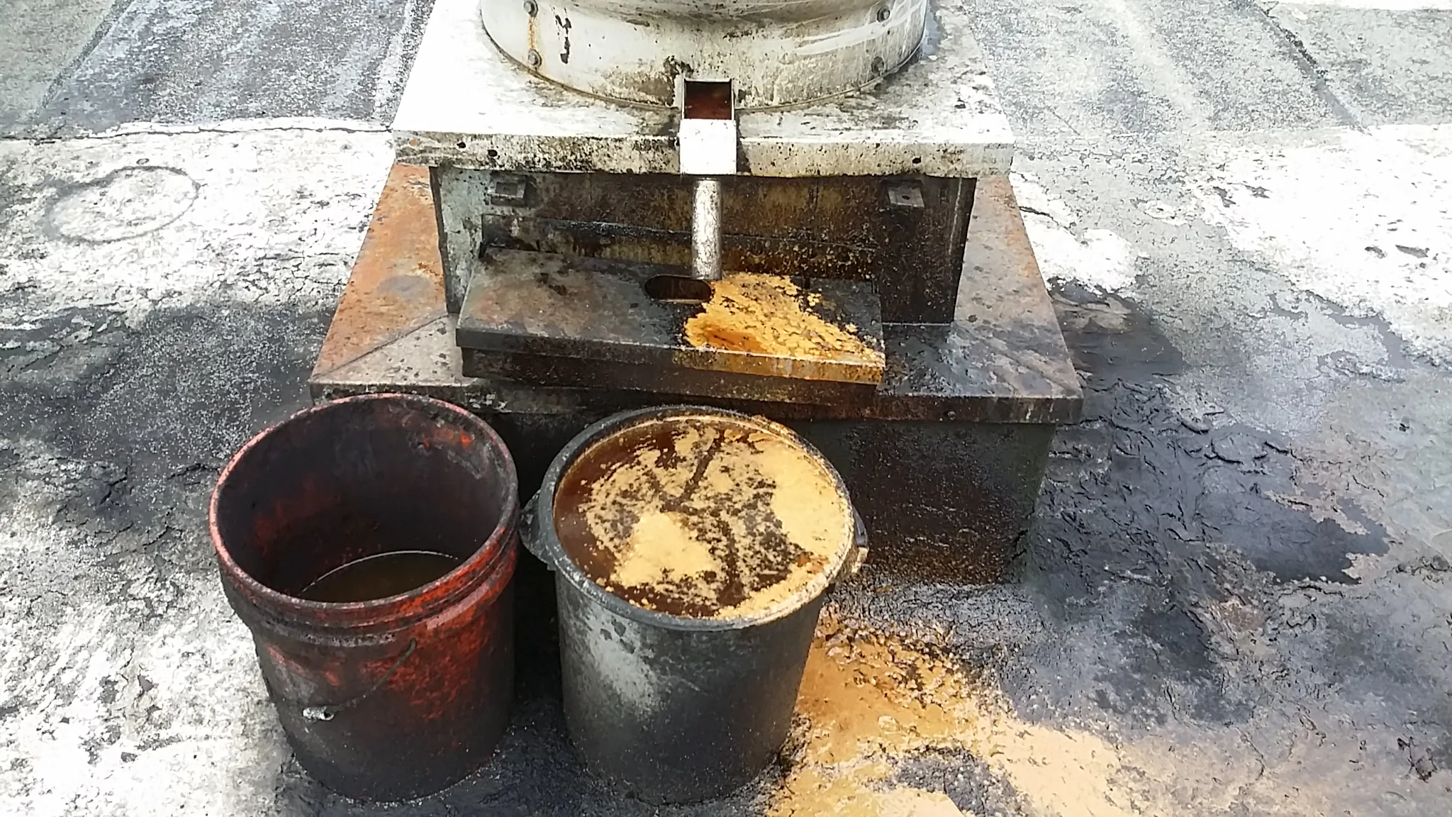 Two buckets of waste grease beside a rooftop containment unit
