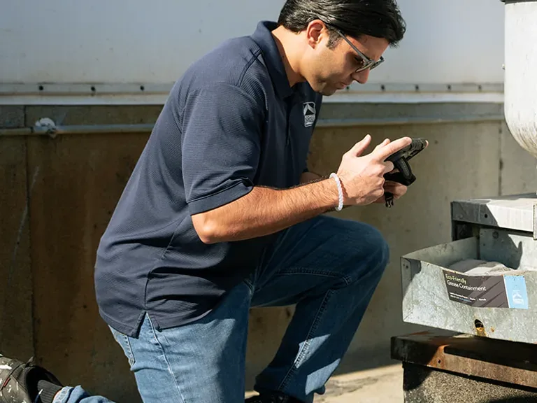 A RoofingSource Field Advisor kneeling at a rooftop unit, photographing its grease containment tray