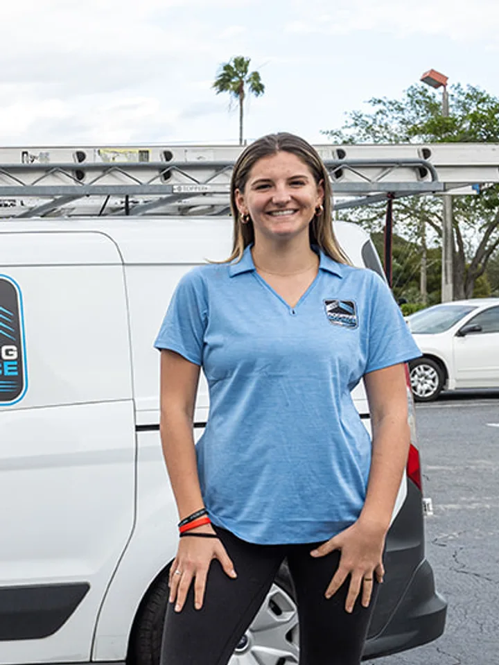 A smiling RoofingSource teammate in a company polo beside a company van