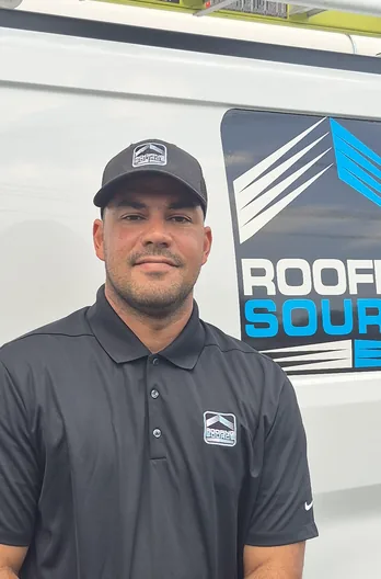 A RoofingSource teammate in a cap and polo standing beside a company van