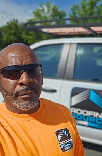 A RoofingSource teammate in an orange shirt standing beside a company van
