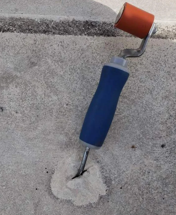 A seam probe hooked under a lifted spot in a white roof membrane, marking the defect