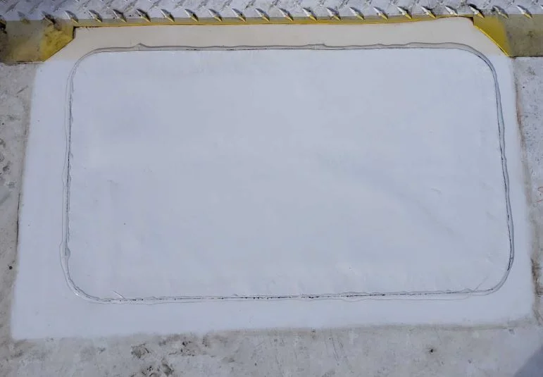 A rectangular welded patch covering the outlined defect beside the curb