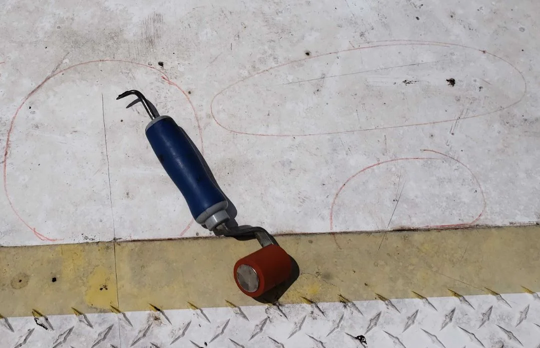 A probe at a membrane defect outlined in grease pencil beside a roof curb